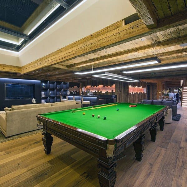 Rustic billiard room with exposed wooden beams, green felt pool table, and modern lounge area.