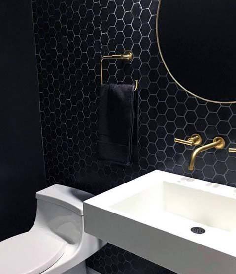 Modern black bathroom with hexagonal tiles, gold fixtures, and a white sink.