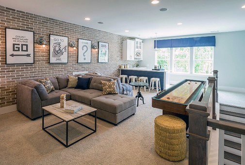Modern family room with sectional sofa, shuffleboard table, brick accent wall, and home bar.