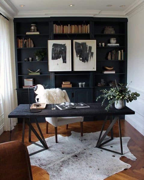 Modern home office with dark bookshelves, abstract art, black desk, and a cowhide rug