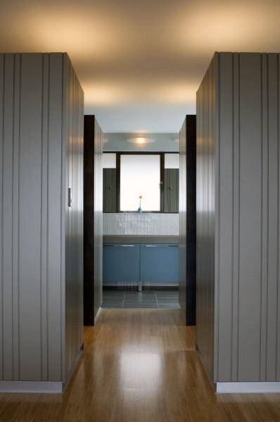 Hallway with vertical paneling, light wood flooring, and minimal white baseboards.