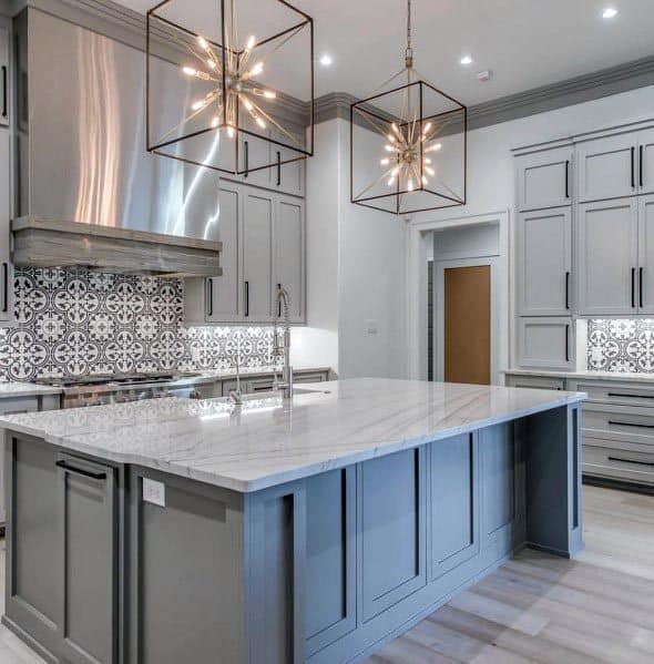 Modern grey kitchen with patterned backsplash, marble countertops, and geometric pendant lights.