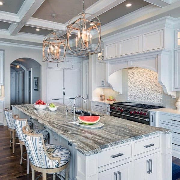 White kitchen with a marble island, ornate pendant lights, and upholstered bar chairs.