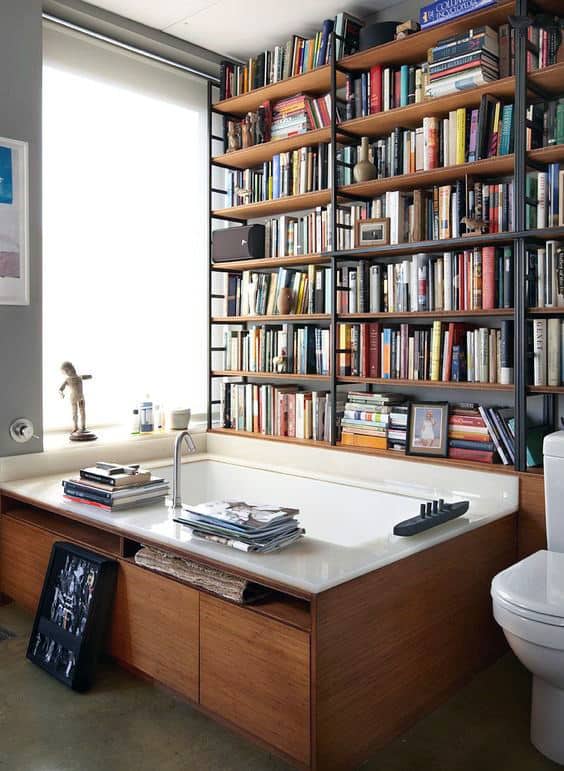 Cozy bathroom with a library vibe: bathtub surrounded by bookshelves and a large window