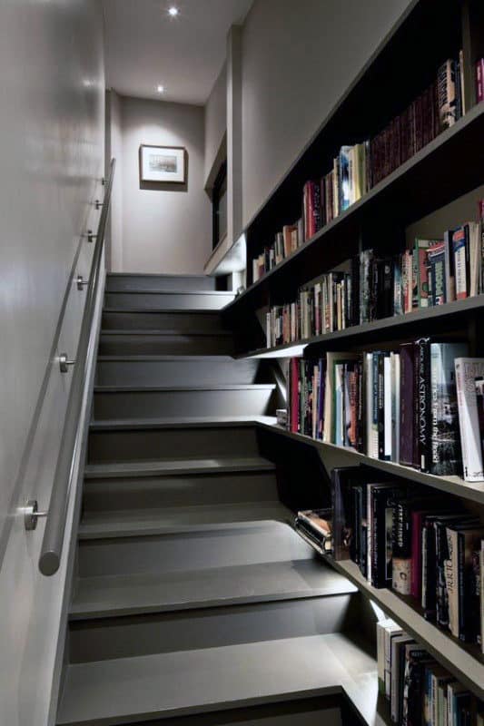 A narrow staircase with library-style shelves on the right leads to a well-lit landing