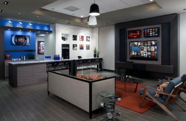 Modern man cave with a large TV, cozy seating, a kitchenette, and sports memorabilia on the walls