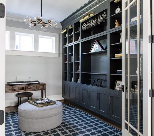 Stylish home office with black built-in bookcases, plaid rug, modern chandelier, and a cozy ottoman centerpiece