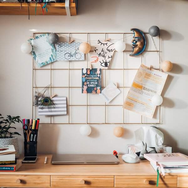 A creative desk setup featuring a wire grid pinboard with personal items, colorful pens, and a plant, creating a motivational workspace.