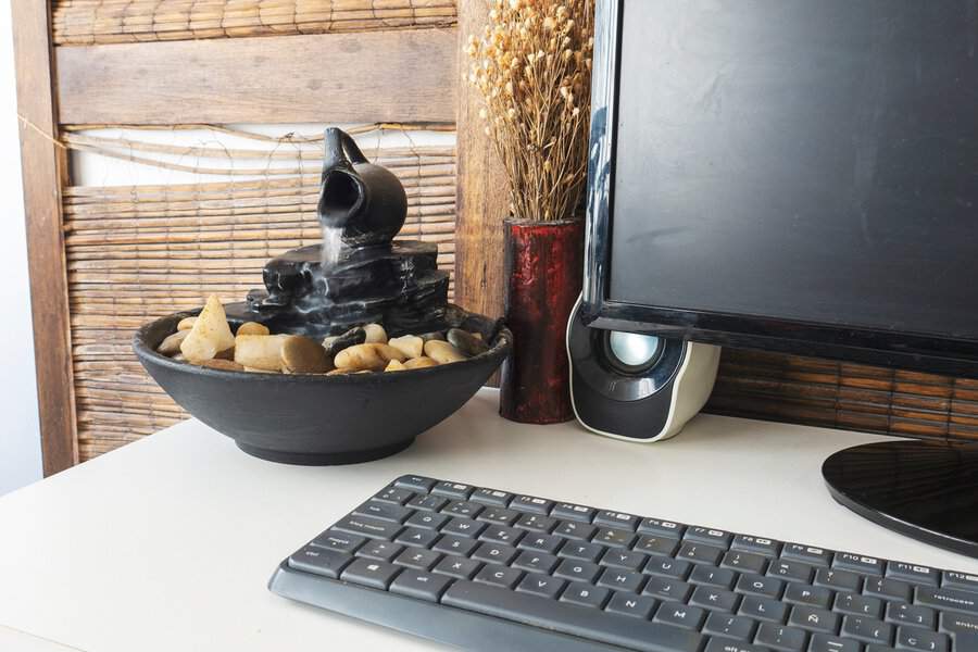 A mini desk fountain with flowing water and stones, creating a calming focal point beside a computer in a home office.
