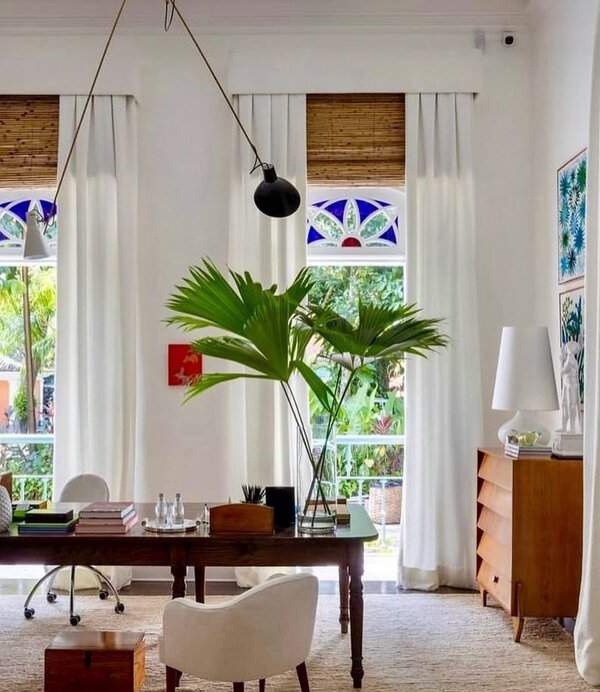 Airy home office with palm leaves, white curtains, bamboo blinds, and stained-glass accents for a lively yet soothing vibe.