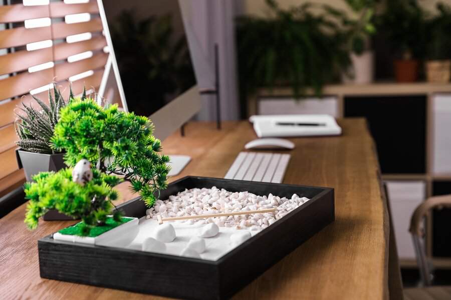 A zen garden with white sand, pebbles, and a bonsai tree creates a peaceful, calming workspace for mindfulness and focus.