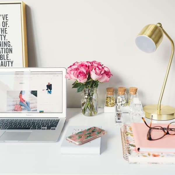 A workspace with a pop of pink from fresh roses, gold accents, and colorful notebooks, creating an energizing and stylish desk setup.