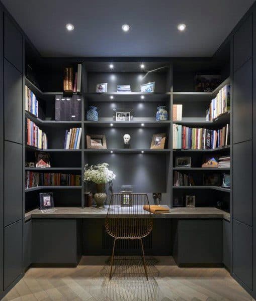 Home office with dark bookshelves, a wire chair, and decorative items under soft lighting