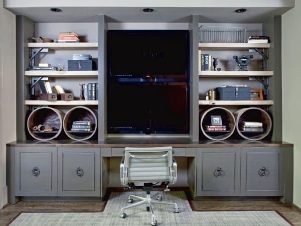 Modern home office with wall shelves, TV, books, decor items, and a white chair at a built-in desk