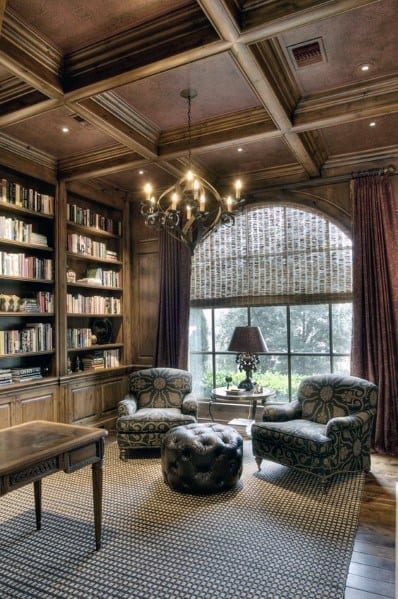 Home library seating area with two patterned armchairs, a tufted leather ottoman, and a round side table.