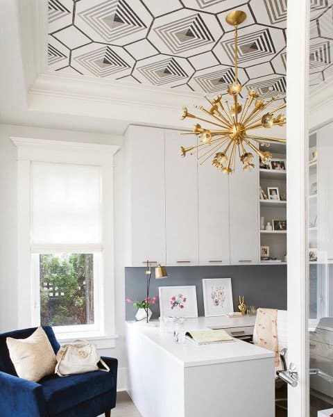 Bright home office with geometric ceiling design, gold chandelier, and white furniture.