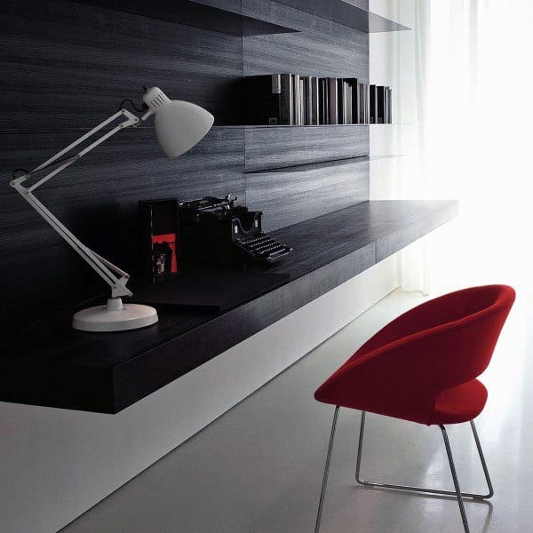 Minimalist home office with black floating desk, red chair, and sleek wall shelves.