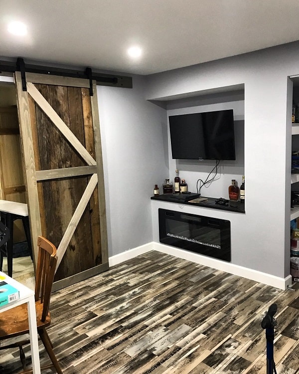 Rustic wood sliding barn door with diagonal cross design in a home office with wood-patterned flooring and wall-mounted TV.
