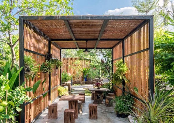 Rustic pergola with bamboo slats, wooden seating, and lush greenery in a serene outdoor setting.