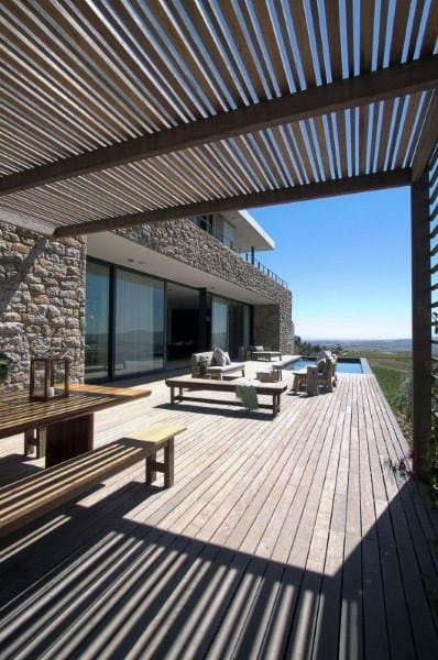 Modern pergola with slatted wood roof, large patio, stone walls, and scenic outdoor views.
