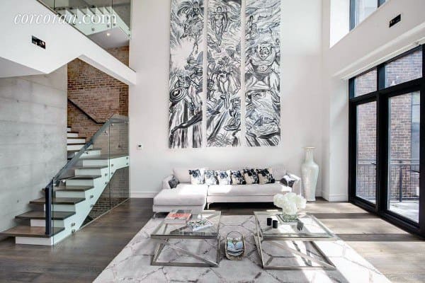 Modern living room with high ceilings, abstract wall art, glass staircase, and a sleek white sectional sofa