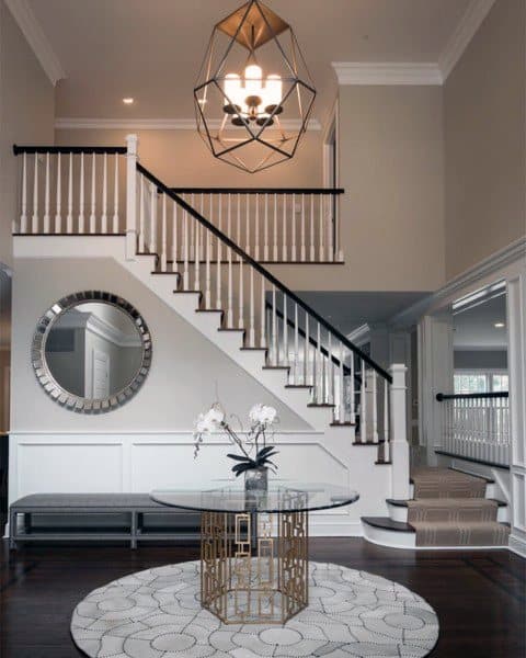 Elegant hallway with a sweeping staircase, round table with orchid, large mirror, and geometric chandelier