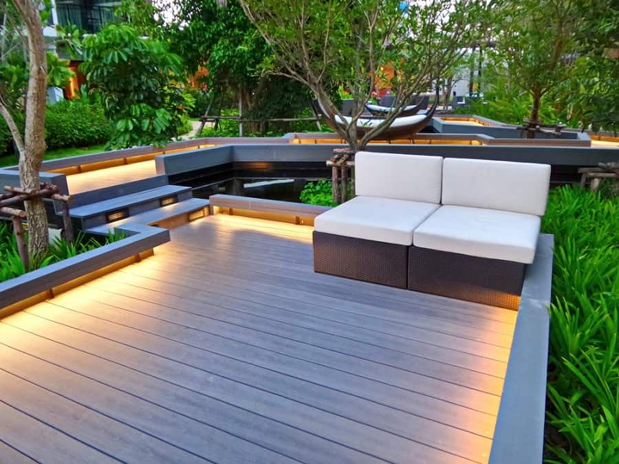 Modern outdoor seating area with illuminated decking, lush greenery, and a stylish walkway