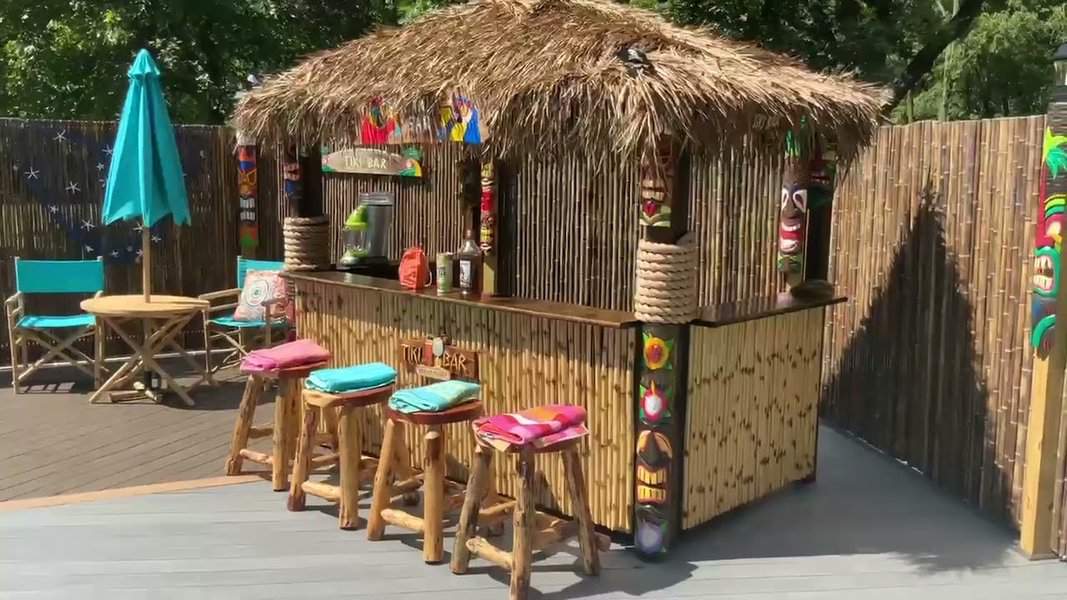 Luxurious tiki bar with thatched roof, wooden stools, and colorful tropical decor.