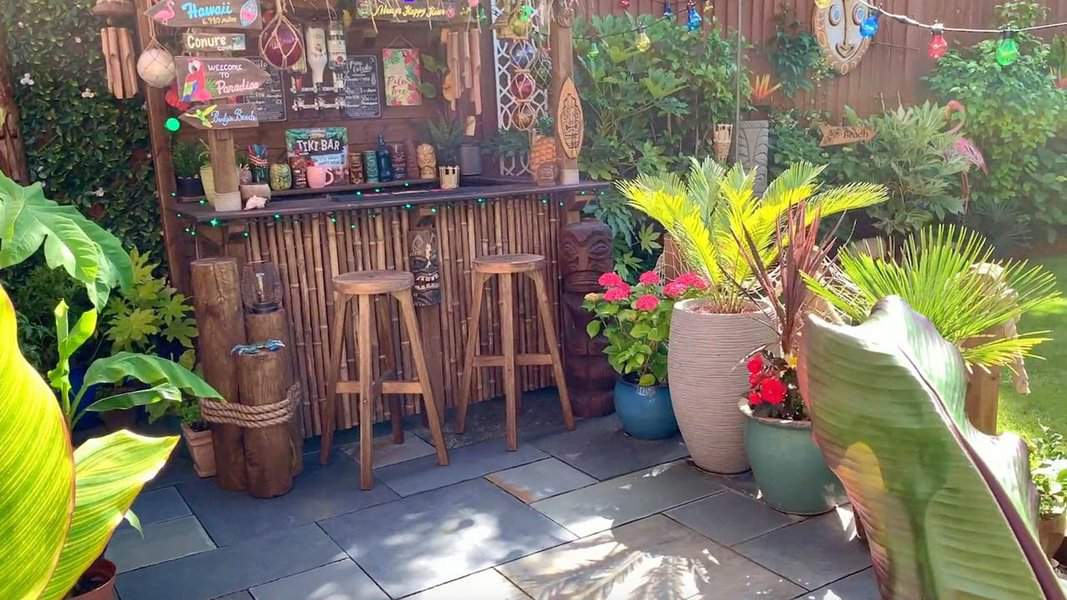 Tropical homemade tiki bar with bamboo stools, colorful decor, and lush plants.