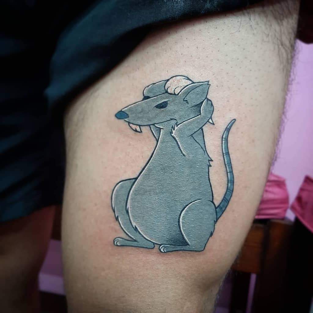 A colorful tattoo of a rat with small curled horns, giving it a devilish look, placed on the upper thigh in a bold cartoon style.