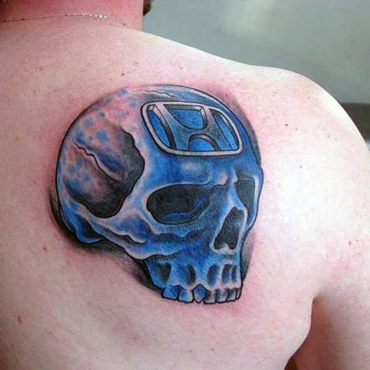 Blue skull tattoo with a Honda logo on a man's shoulder, featuring bold shading and a fiery effect for a striking design.