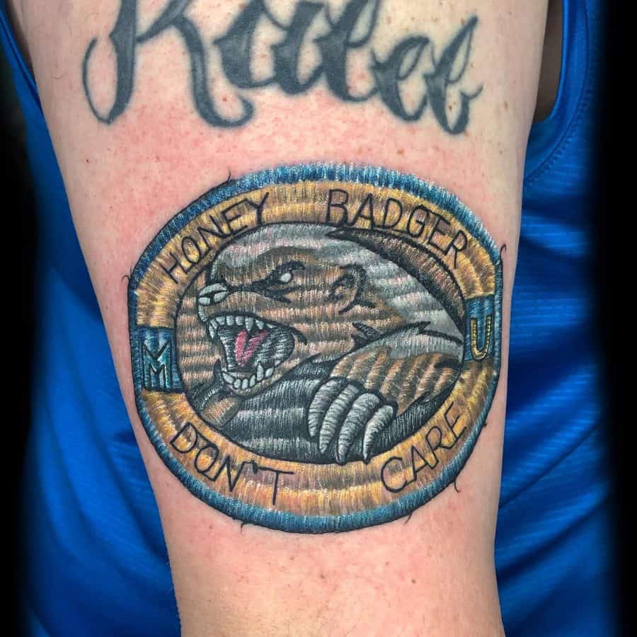 Textured patch-style tattoo featuring a roaring honey badger with bold stitched details and embroidered lettering.