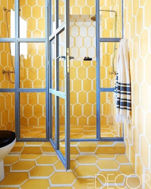 Bathroom with honeycomb-patterned yellow tiles, steel-framed shower enclosure, and brass fixtures for a dynamic geometric look.