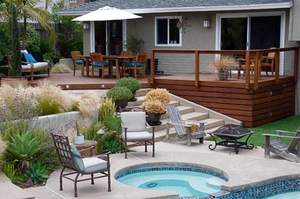 large backyard pool raised wood deck with dining furniture and wood railing