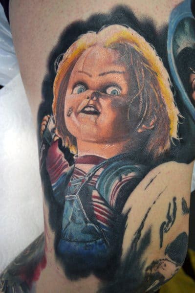 Realistic Chucky tattoo with vivid colors, featuring his eerie grin, wide blue eyes, and detailed shading for a bold horror-inspired design.