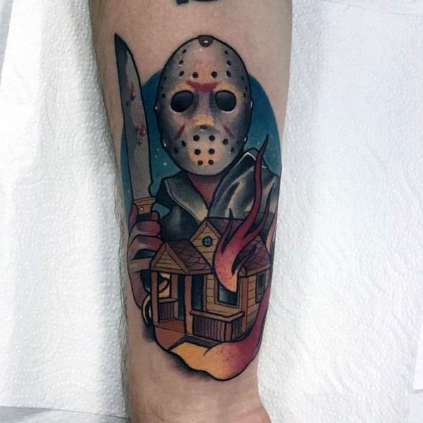 Horror tattoo featuring a masked killer with a bloody knife, standing over a burning house under a dark night sky.