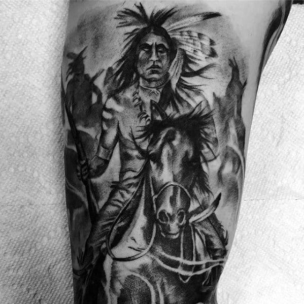 Black and grey tattoo of a Native American warrior on horseback holding a spear, surrounded by shadowy figures and dynamic shading