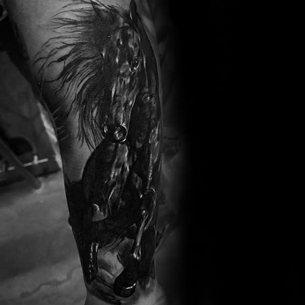 Dark and dramatic black and grey tattoo of a rearing horse with intense highlights and flowing mane, placed on the upper arm or forearm