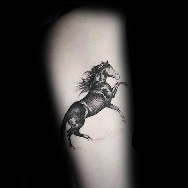 Dotwork-style tattoo of a rearing horse with flowing mane, placed on the upper arm or thigh with soft shading and fine detail