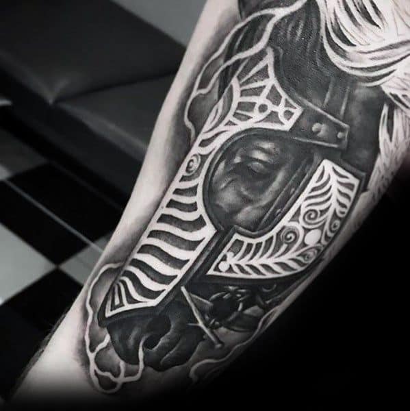 Black and grey tattoo of a horse wearing ornate medieval armor, featuring intricate detailing and bold shading on the forearm