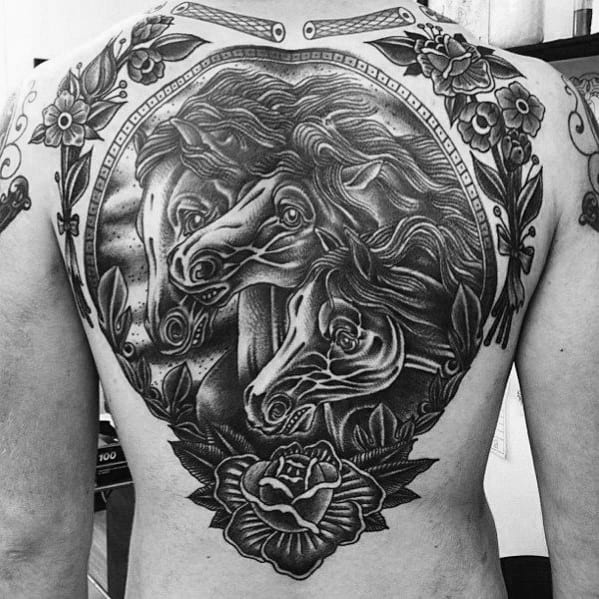 Black and grey full back tattoo of three detailed horse heads framed by roses, leaves, and ornate decorative elements