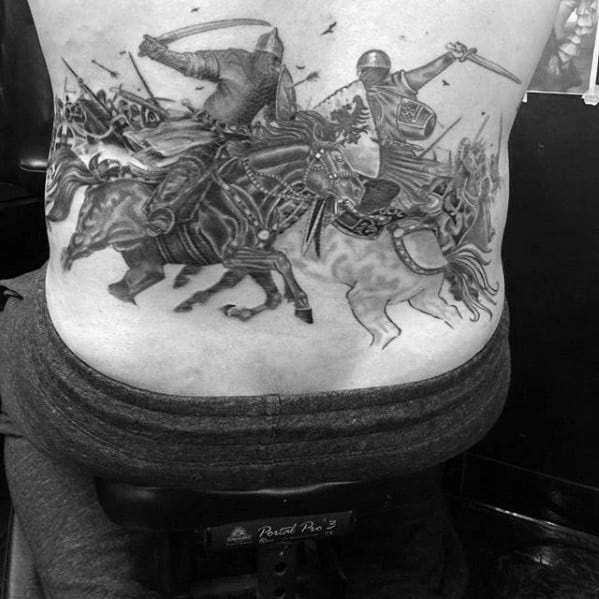 Black and grey lower back tattoo of two armored warriors in mid-battle on horseback, surrounded by a cavalry charge and flying arrows