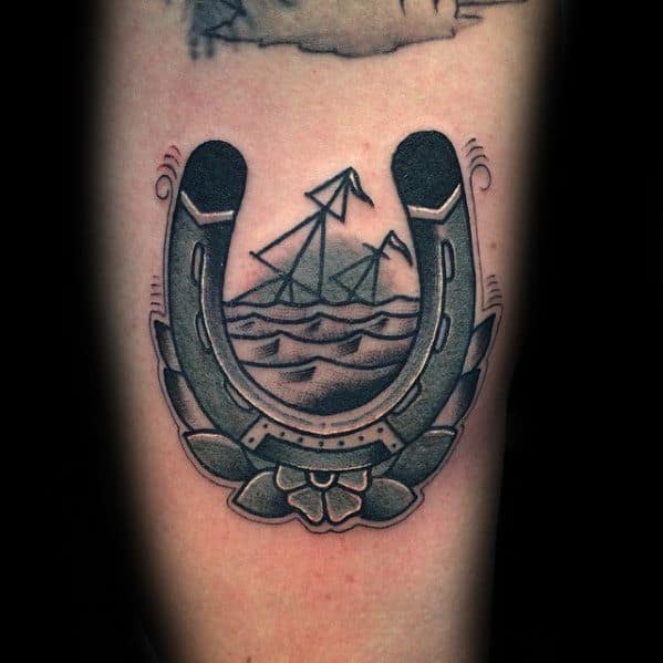 Traditional-style tattoo of a sinking ship inside a horseshoe frame with waves, laurels, and a flower at the base for a bold nautical look.