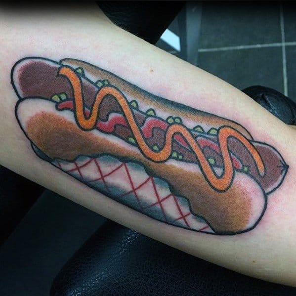 Tattoo of a hot dog with mustard and relish inside a bun, with bold outlines and vibrant colors on the forearm.