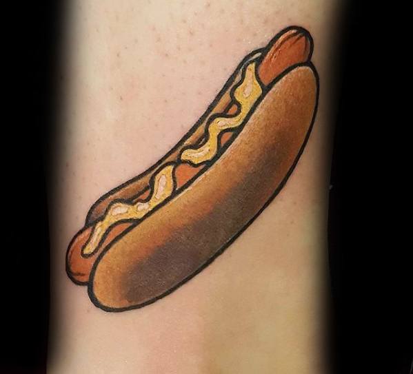 Simple and colorful hot dog tattoo featuring a sausage with mustard in a soft bun on the forearm.