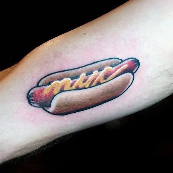 Realistic hot dog tattoo with mustard on a sausage inside a soft bun on the forearm.