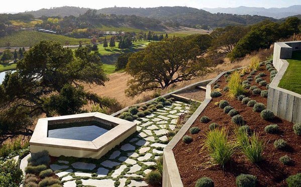 Modern hillside landscaping with a geometric hot tub, stone pathway, drought-tolerant plants, and stunning valley views