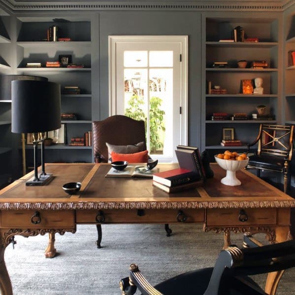 Classic home office with built-in bookcases, ornate wooden desk, leather chair, and natural light through French doors