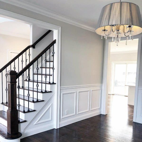 Modern interior with dark wood staircase, chair rail wainscoting, and large chandelier, doorway leads to bright room