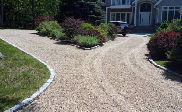 Curved gravel driveway with stone edging, leading to a landscaped entrance of a home.